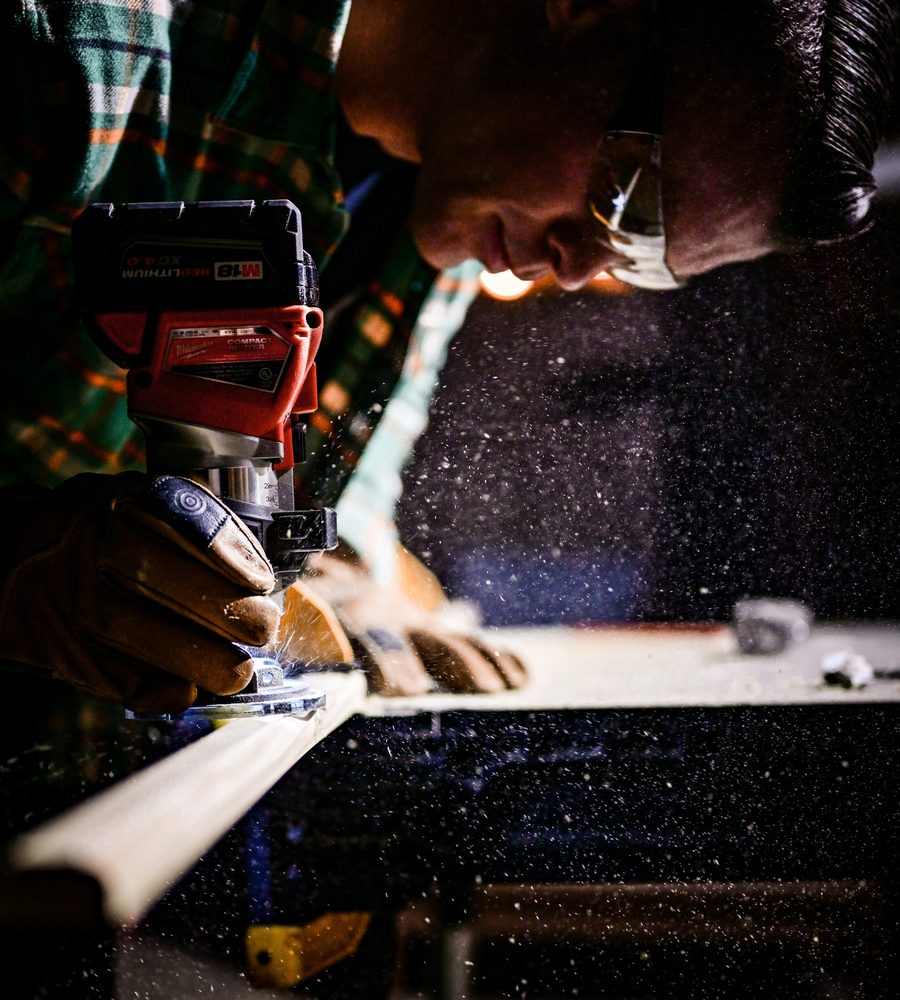 Carpenter running a router along a length of timber, sawdust in the air
