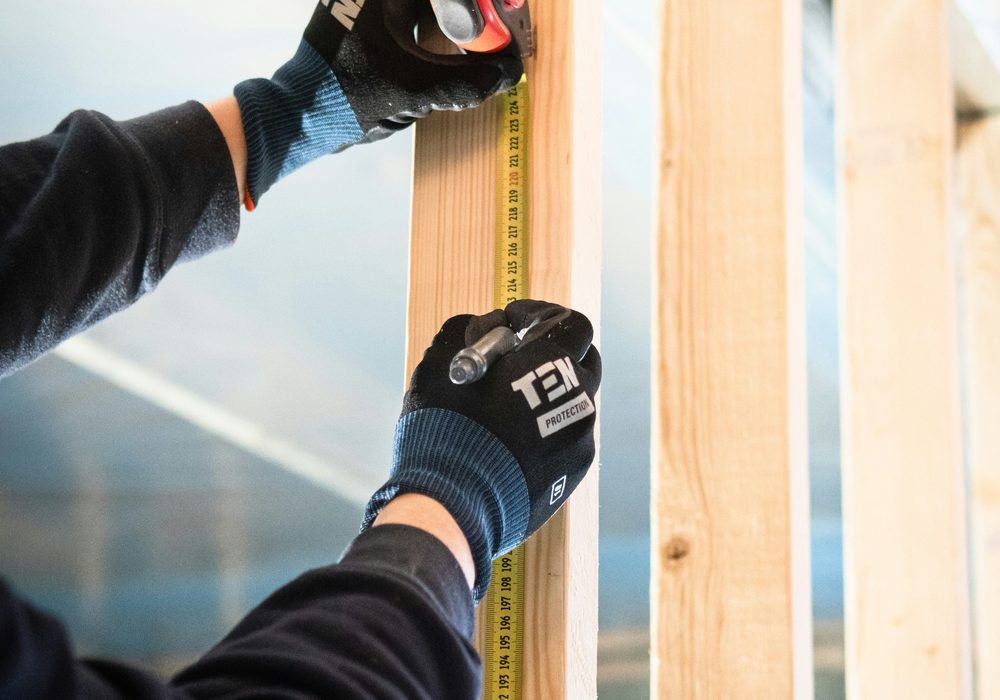 Gloved hands measuring a timber stud in a framed wall